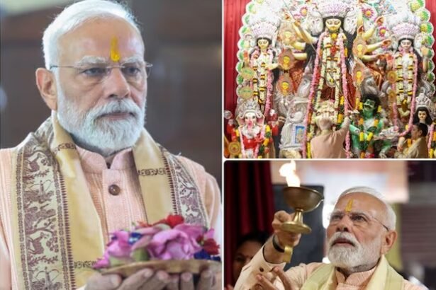 प्रधानमंत्री नरेंद्र मोदी दिल्ली के सीआर पार्क दुर्गा पूजा पंडाल में मां दुर्गा की आरती करते हुए, पीछे सजीव मूर्ति और भक्तों की भीड़।