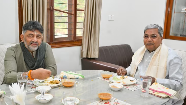 सिद्धारमैया और डीके शिवकुमार एक टेबल पर बैठकर बातचीत करते हुए ब्रेकफास्ट मीटिंग में शामिल हैं।