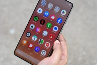 मोबाइल फोन स्क्रीन पर साइबर सुरक्षा ऐप दिखाते हुए व्यक्ति, डिजिटल सुरक्षा के प्रतीक आइकॉन के साथ।