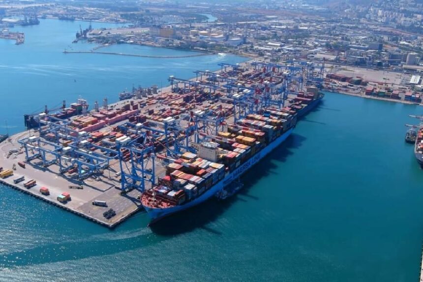 इजरायल के हाइफा बंदरगाह का हवाई चित्र, जहाज लंगर डाले, कंटेनर स्टैक, समुद्र तट पर। अडानी लोगो दिखे।